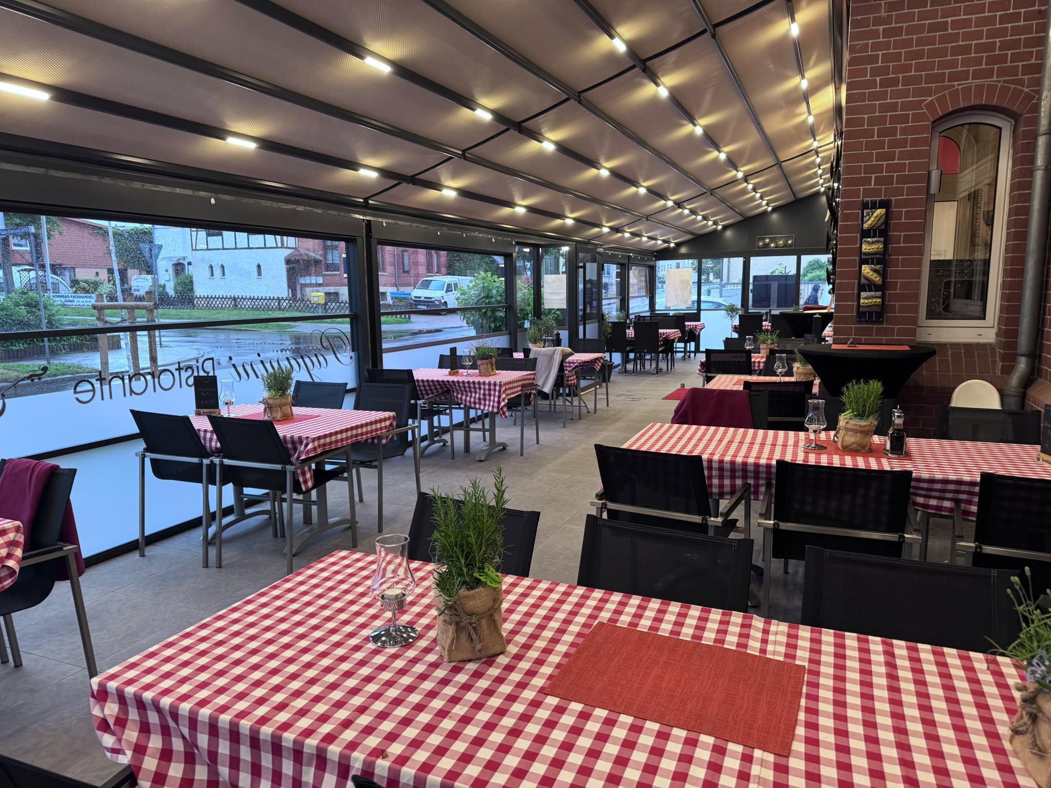 Überdachte Terrasse mit rot-weiß karierten Tischdecken und Rosmarin-Töpfen
